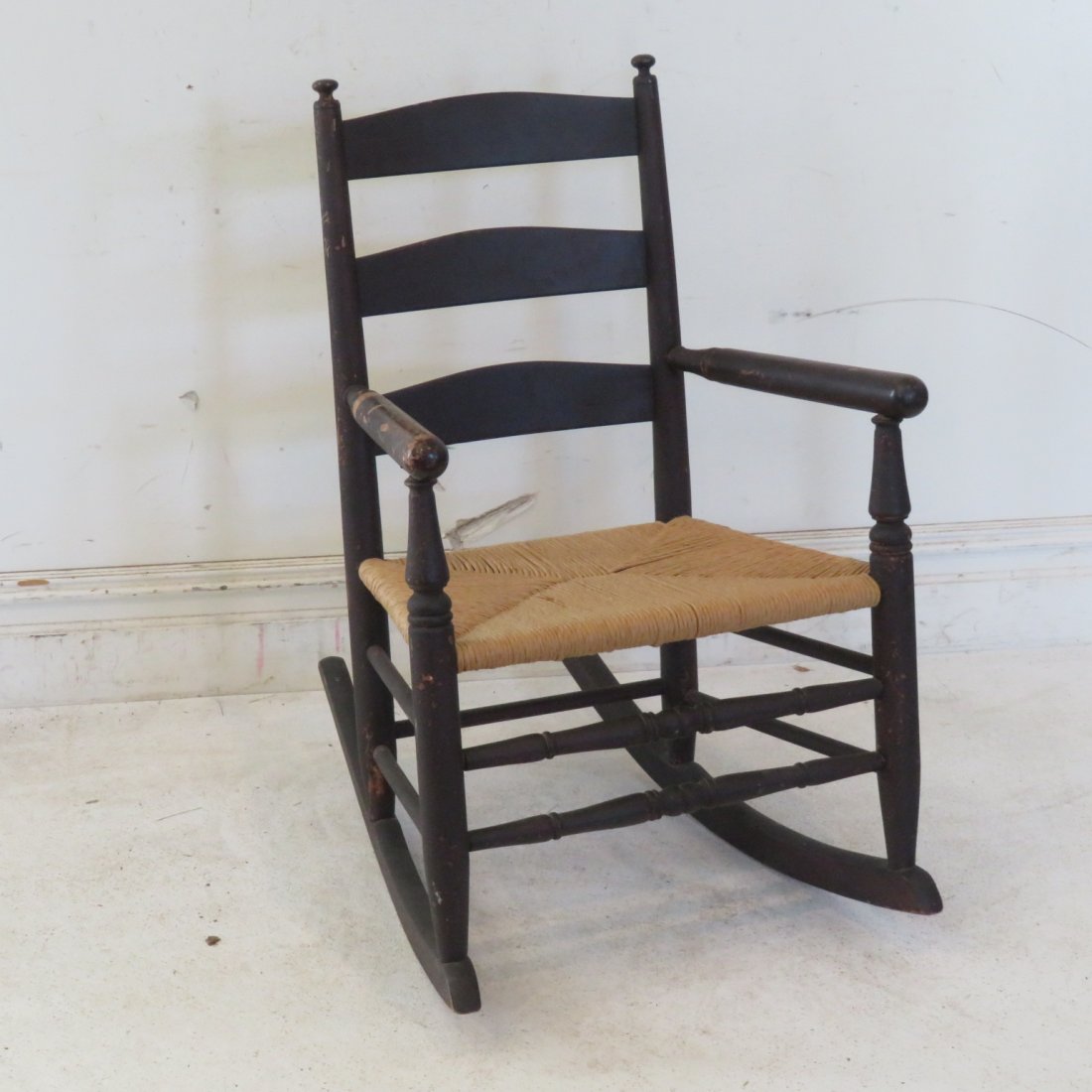 Country ladderback rocker: Country ladderback rocker in old black painted surface, good rush seat, 32" t., seat 16" x 18"