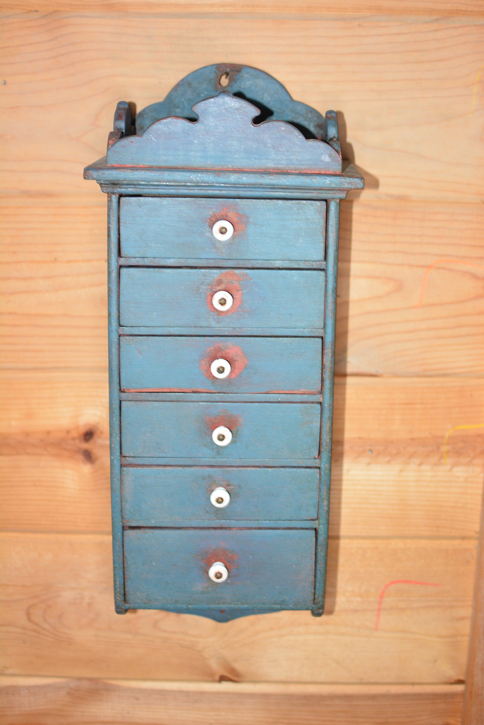 Hanging Set of Six Drawers: Hanging Set of Six Drawer in old blue paint over red w/ porcelain knobs w/ gallery. Back retains old red paint 9"W x 6"D x 22"T.From the Collection of Roselyn Potts.