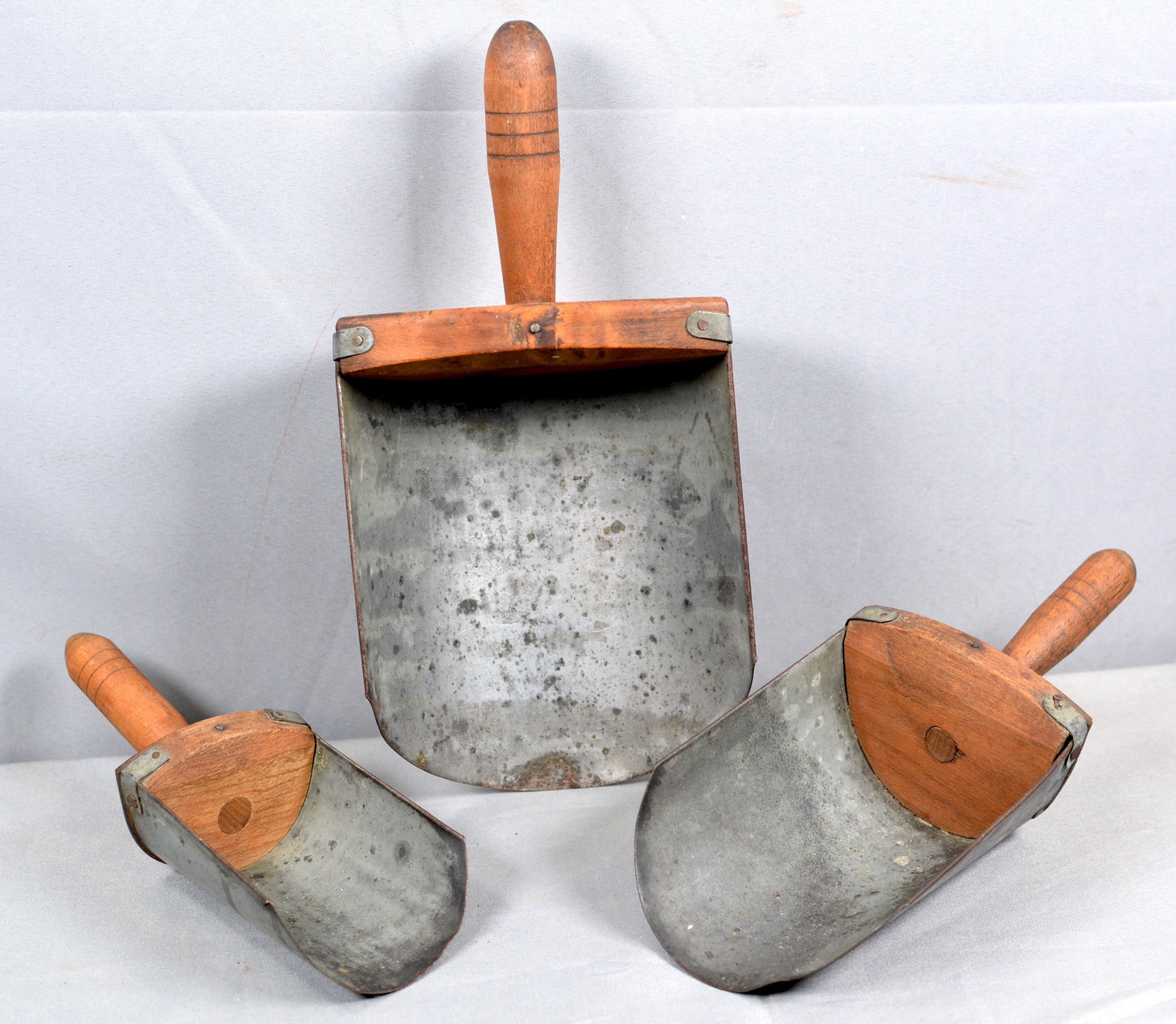 Three Tin & Wood Graduated Size Scoops: Three tin & wood graduated scoops w/ wooden handle that have 3 incised lines. Smallest 3" W x 9"T Middle 4 1/2"W x 10" Largest 6"W x 12"T