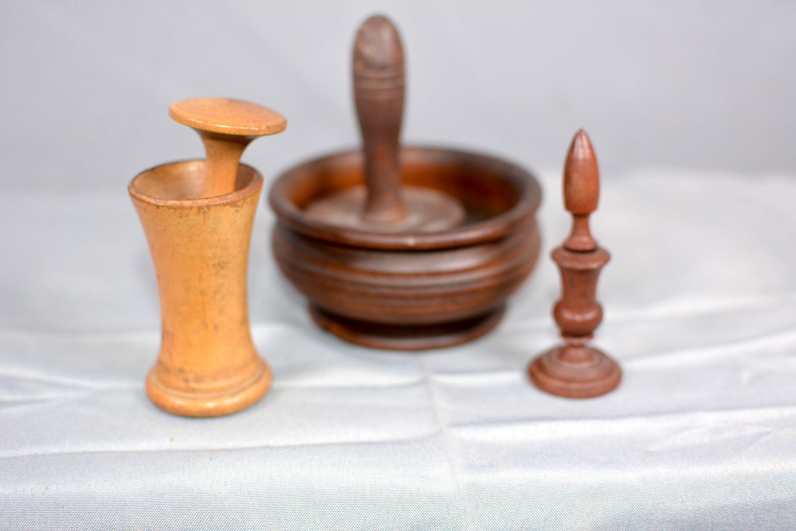 Three Pieces of Treenware Kitchenware: 2 Wooden herb grinder one is marked Burns New York & straight pin w/ wooden finial & base. Largest 4"W x 4"T. From the Collection of Roselyn Potts.