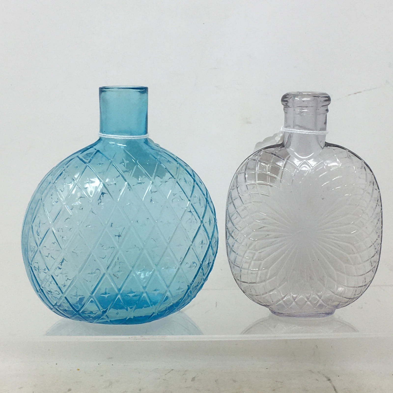 (2) American Glass Liquor Spirit Flasks 1.) Light blue quilted pattern with repetitive cross motif: (2) American Glass Liquor Spirit Flasks 1.) Light blue quilted pattern with repetitive cross motif in the center of each pattern, no cracks or chips, unmarked 5" W x 5.5" H 2.) Light Amethyst sunburst