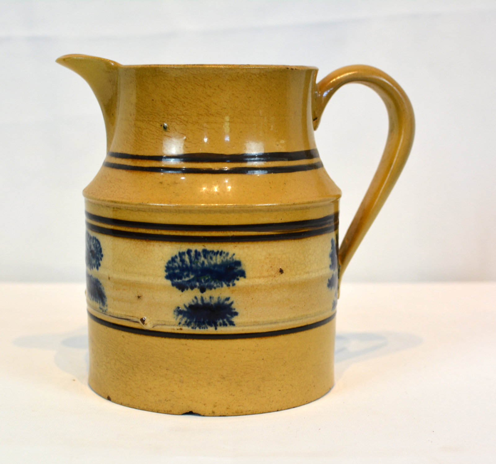 19th Century banded mocha ware pitcher: Early 19th-century English mocha ware pitcher featuring cobalt blue dendritic decoration on a cream-colored slip band framed by black bands. Bottom has crow's feet and top rim has minor roughness.