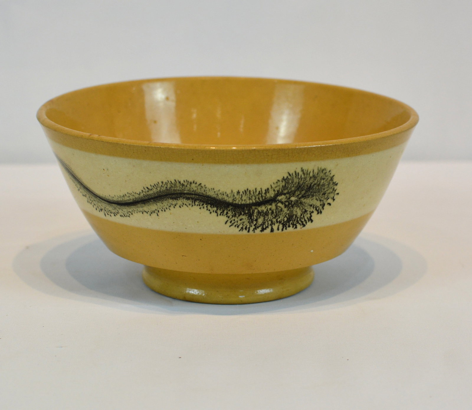 19th Century Mocha Ware Bowl with Green Decoration: Early 19th-century English mocha ware footed bowl with green "seaweed" decoration flowing across a cream-colored slip band. The shallow bowl form on raised neatly formed foot. Size: 6 3/4 in. Dia. x