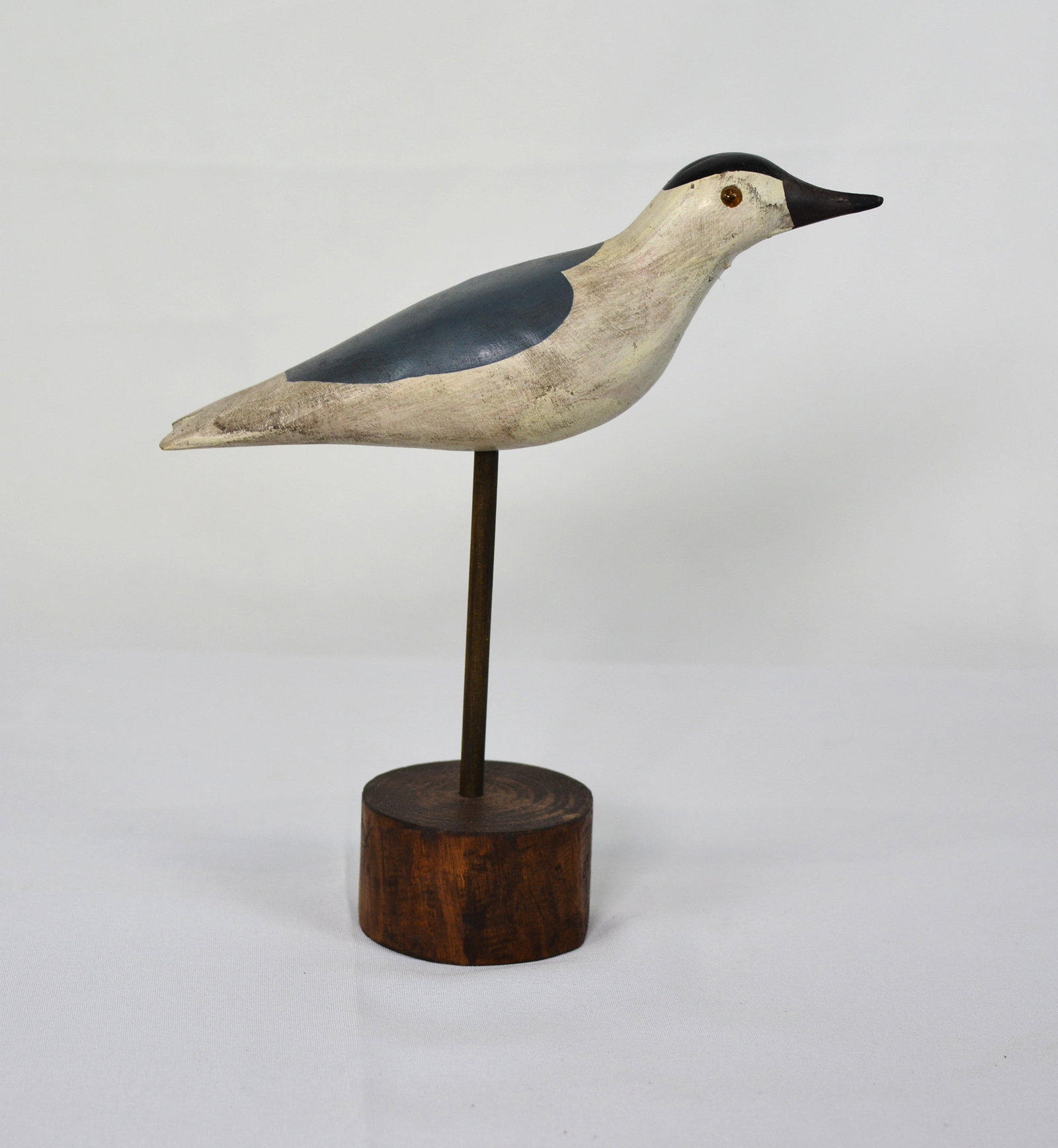 Folk Art Shorebird on stand: Hand-carved and painted shorebird mounted on a turned wooden base. The carving features a clean, minimalist form with black-and-white coloration and glass eyes, coastal waterbird. 8 in. L × 2.5 in.
