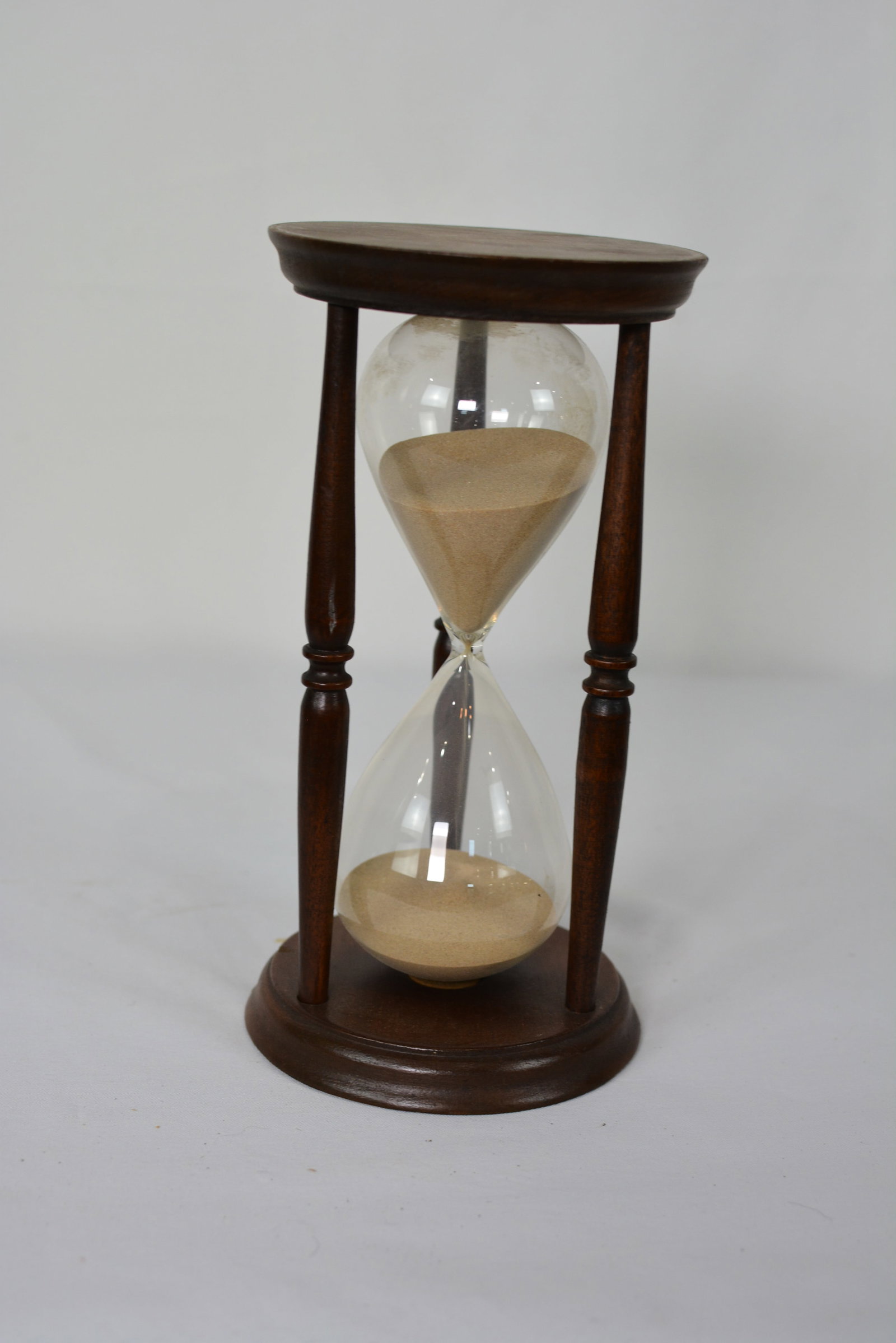 Large Decorative Hourglass in Turned Wood Stand: Large Decorative Hourglass in Turned Wood Stand. Oversized hourglass featuring a clear blown-glass timer with fine sand housed within a turned hardwood frame, classic form is supported by four turned