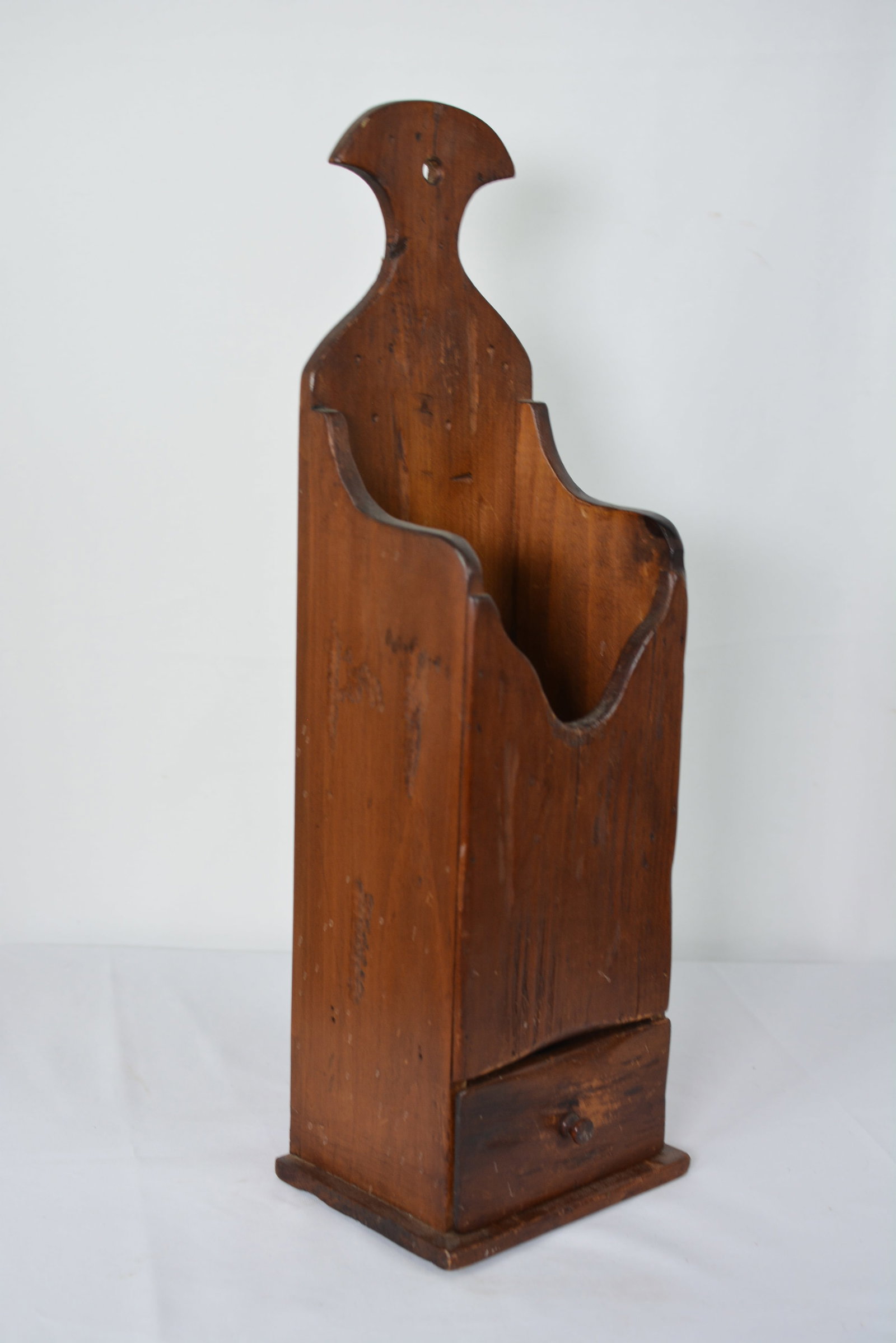 19th Century Wall-Mounted Wooden Candle Box with Drawer: Early wooden wall-mounted candle box featuring a shaped backboard, open storage compartment, and a small lower drawer with turned wooden pull. 18 inches high x 6 inches wide x 4.5 inches deep.
