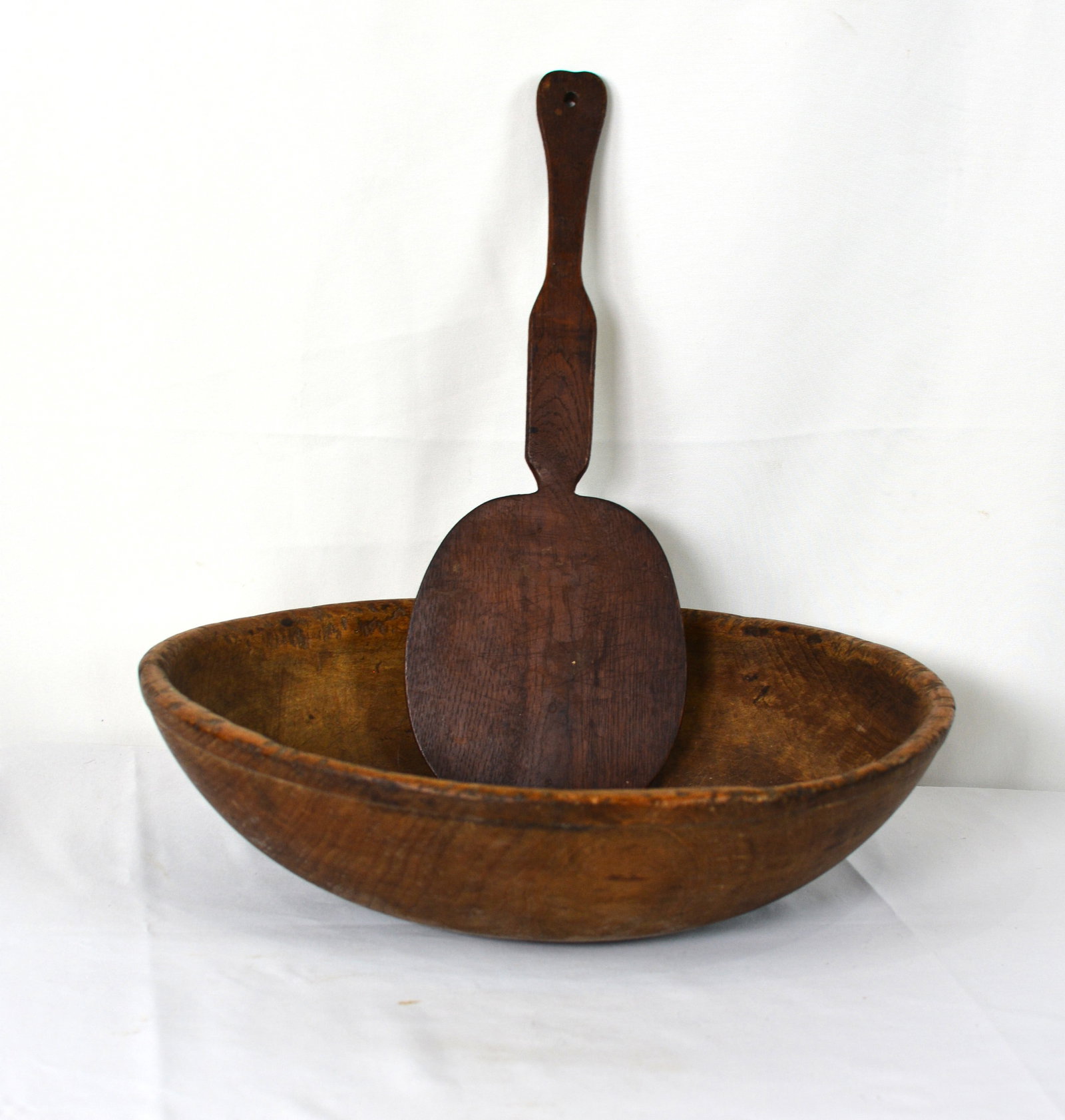 Early Hand-Carved Wooden Dough Bowl and Bread Paddle: Collection of two early American kitchen antiques consisting of a hand-carved wooden dough bowl and a large wooden bread paddle or peel. Dough Bowl: 15 inches long x 13 inches wide x 5.5 inches high.