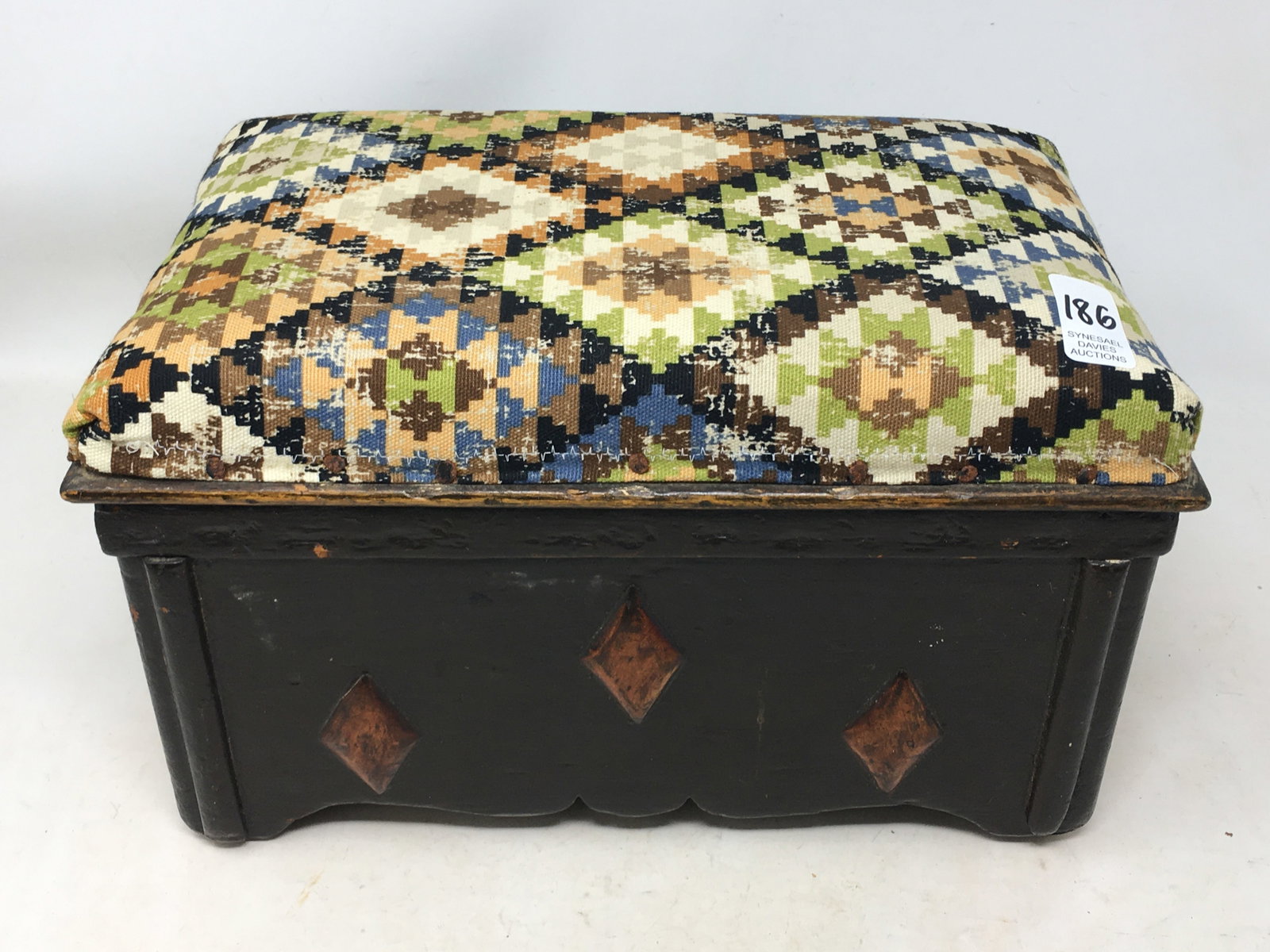 Carved Padded Footstool: Carved Padded Footstool. Wooden box-shape footstool with carved ends having diamond shapes around sides. Padded top in a geometric design fabric. 12"L x 7.25"W x 7"H.