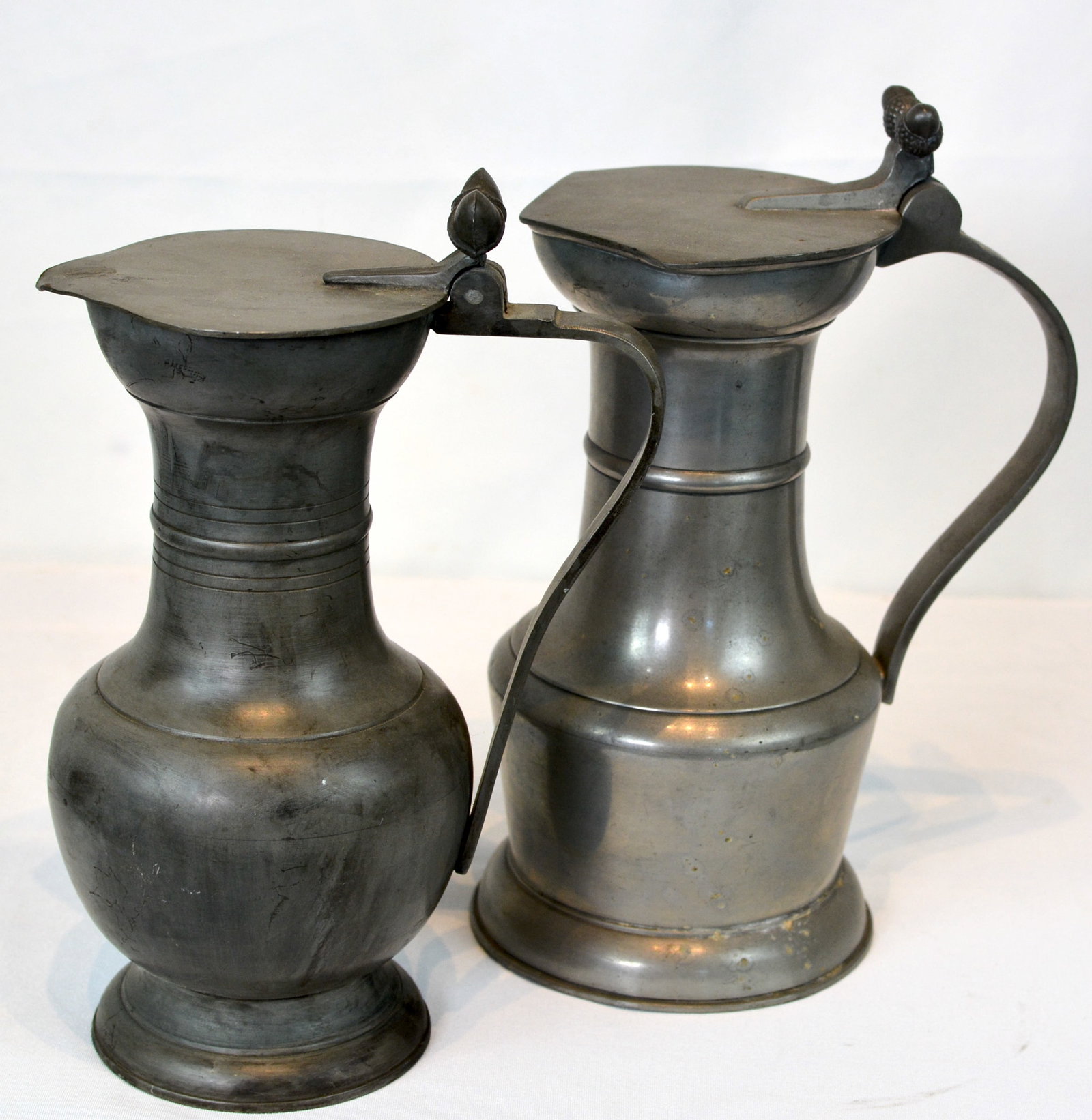 Pair of Pewter Lidded Tavern Measures: Pair of pewter lidded tavern measures, late 18th to early 19th century. Each featuring a hinged lid with thumbpiece, tapered handle, and molded body. 8 in. H.