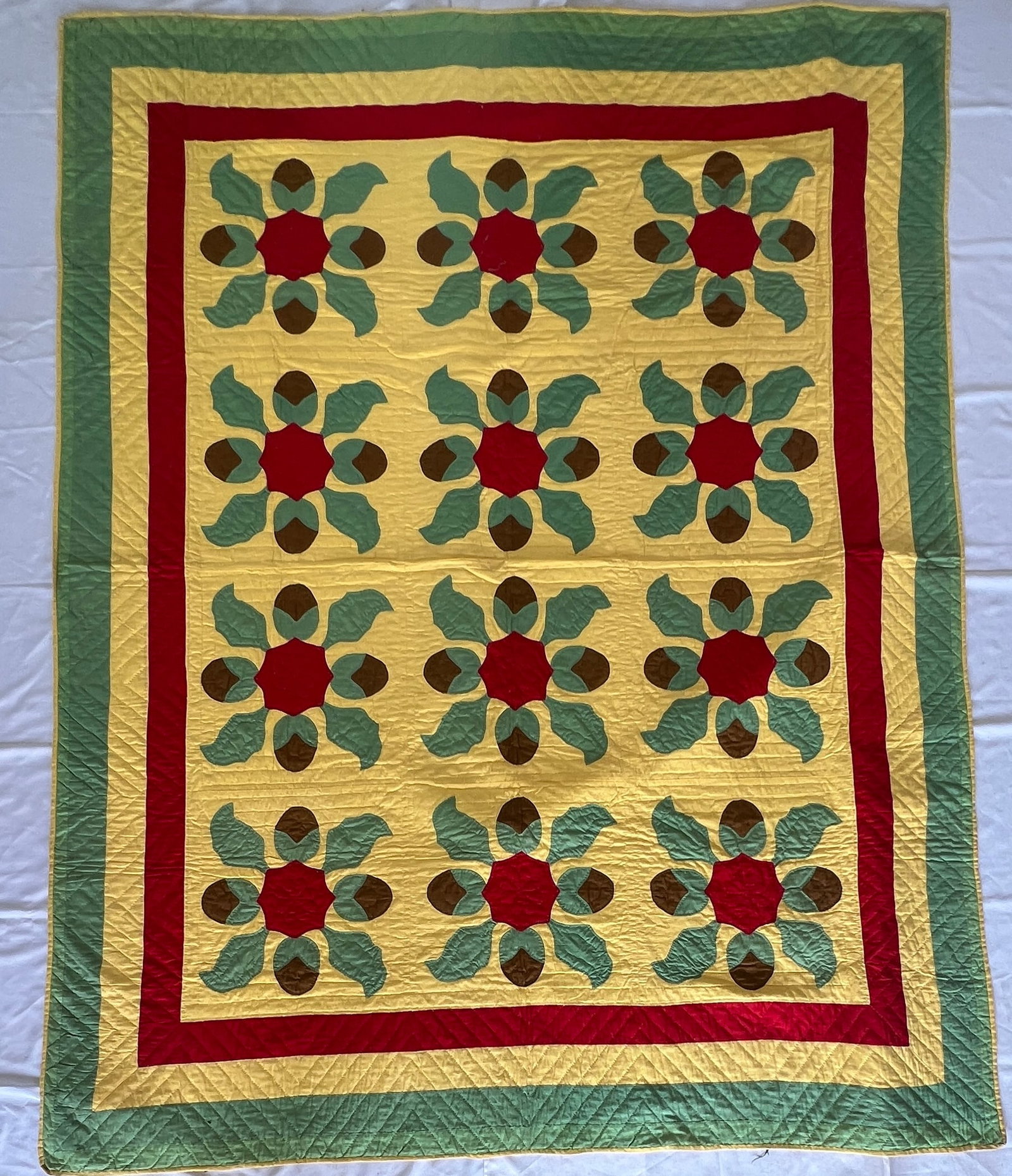 Hand-Stitched Floral Appliqué Quilt: Colorful hand-stitched quilt featuring twelve floral appliqué blocks arranged in a four-by-three pattern. The design showcases vibrant red flower centers with green leaves and brown accents set again