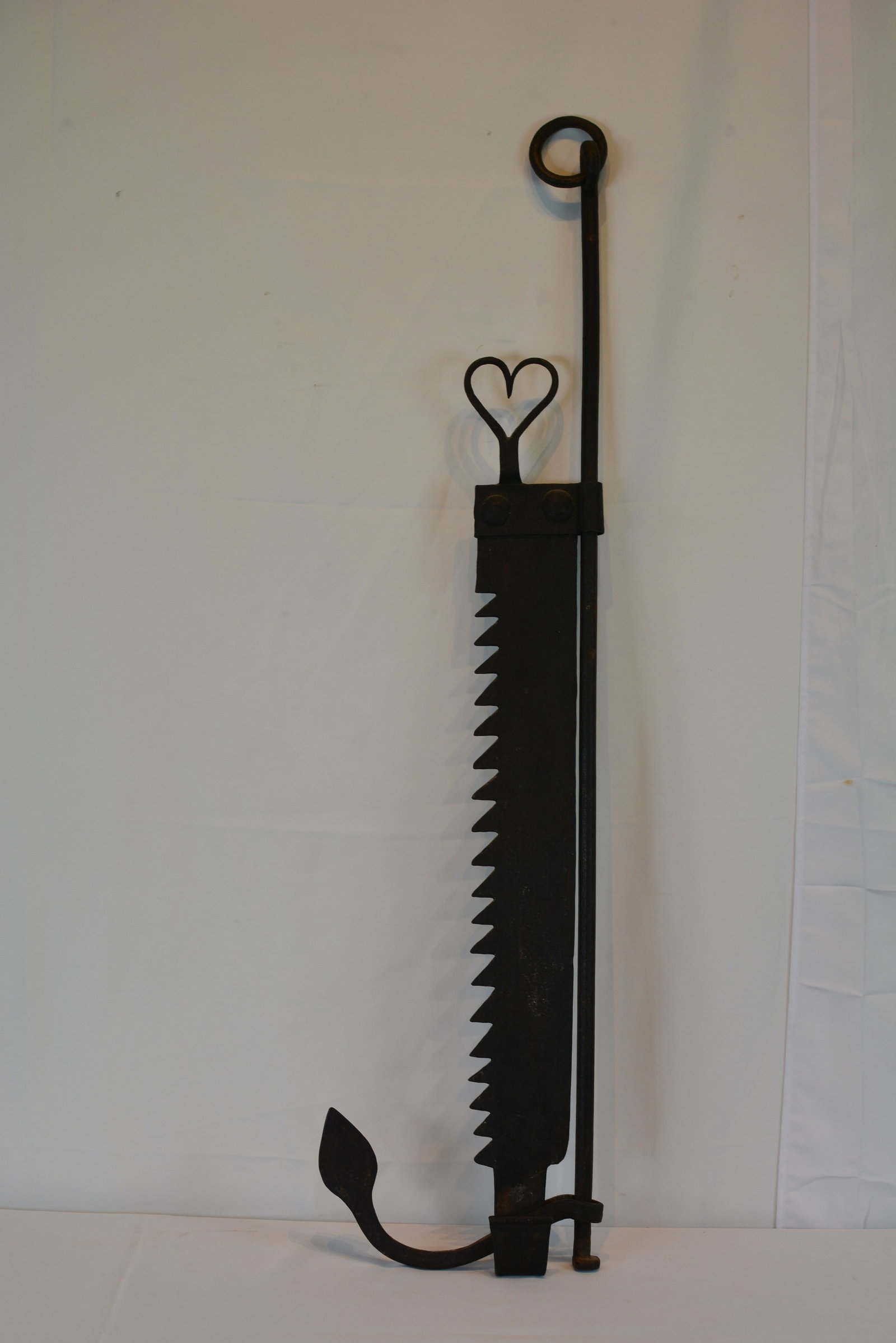 19th Century Wrought Iron Adjustable Hearth Trammel: Early hand-forged wrought iron hearth trammel, ratcheted adjustment bar, heart-form hanger, and forged hook. 41 in. H x 10 in. W.