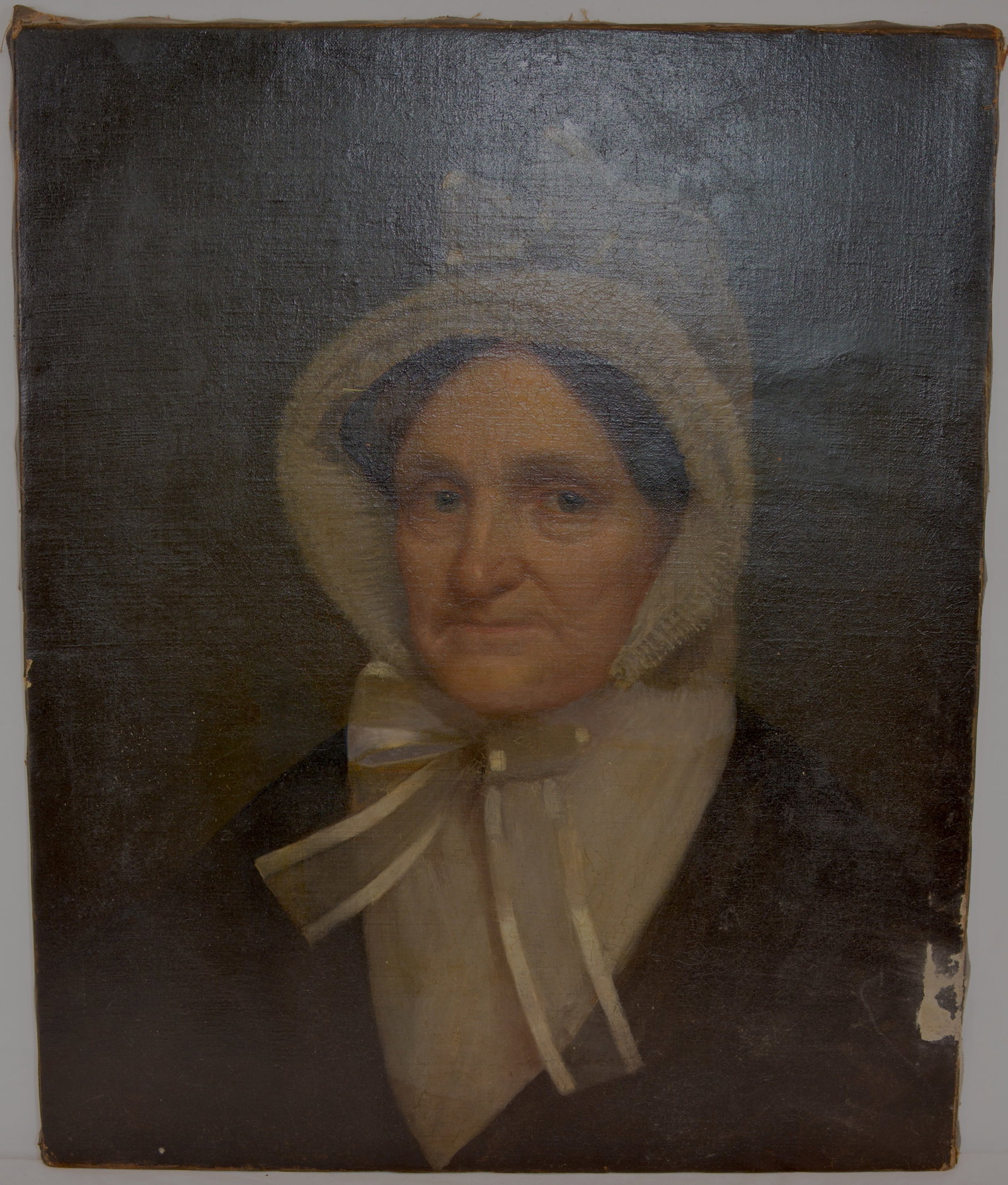 American Folk Art Portrait of a Woman in White Bonnet, Oil on Canvas, Dated 1836: American School, 19th Century oil on canvas portrait depicting an elderly woman wearing a white bonnet and sheer ribbon-tied collar against a dark background. A handwritten inscription visible on an a
