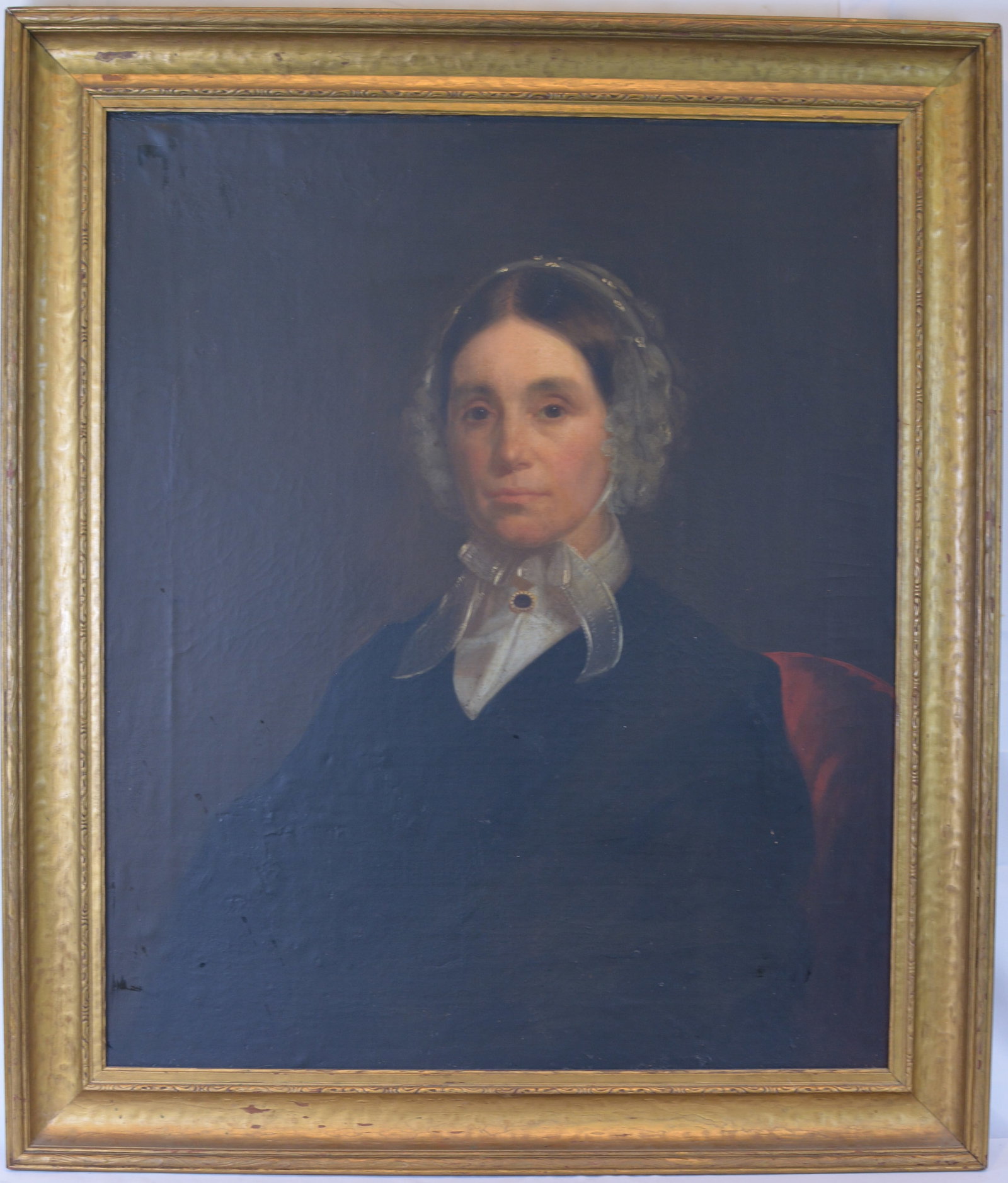 Large 19th Century American Folk Portrait of a Seated Lady in Original Gilt Frame: Mid-19th century American oil on canvas portrait depicting a seated woman dressed in a dark gown with a white lace bonnet and collar, accented by a decorative brooch at the neck. Executed in the folk