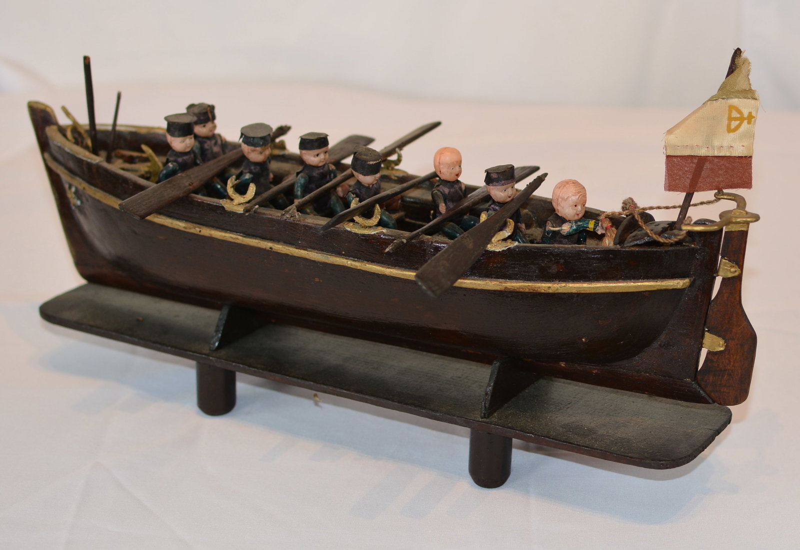 Folk Art Carved Naval Crew Rowing Boat Diorama on Stand: Folk art hand-carved rowing boat diorama depicting a crew of sailors seated at their oars. Crafted in wood and mounted on a custom display stand, the model features individually carved figures,