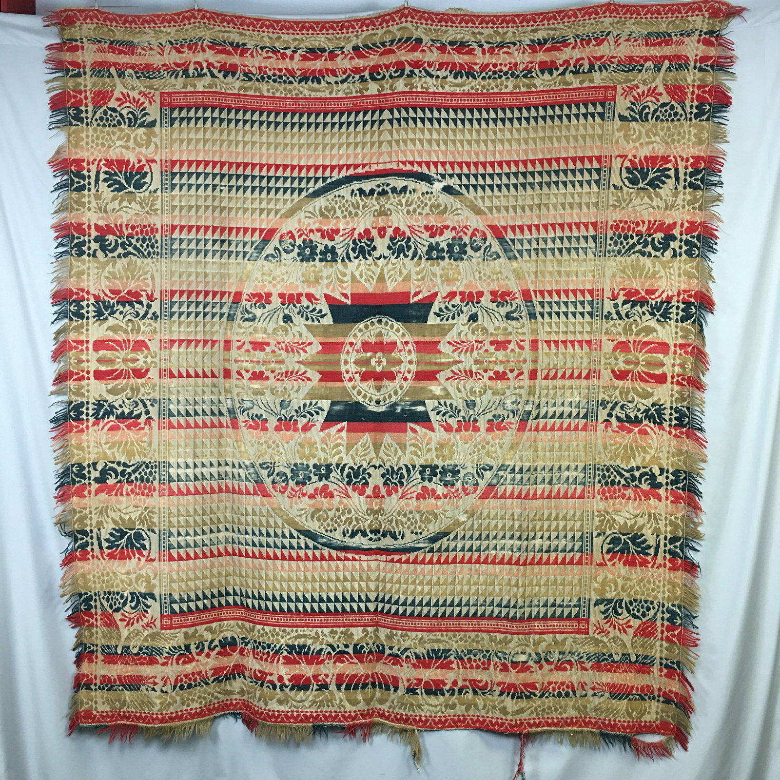 Four Color Woven Coverlet: Four color woven fringed coverlet with a central floral medallion surrounded by a square of arrows/flying geese pattern. The edges feature a scroll and grapevine pattern, with corner eagles. Fringed