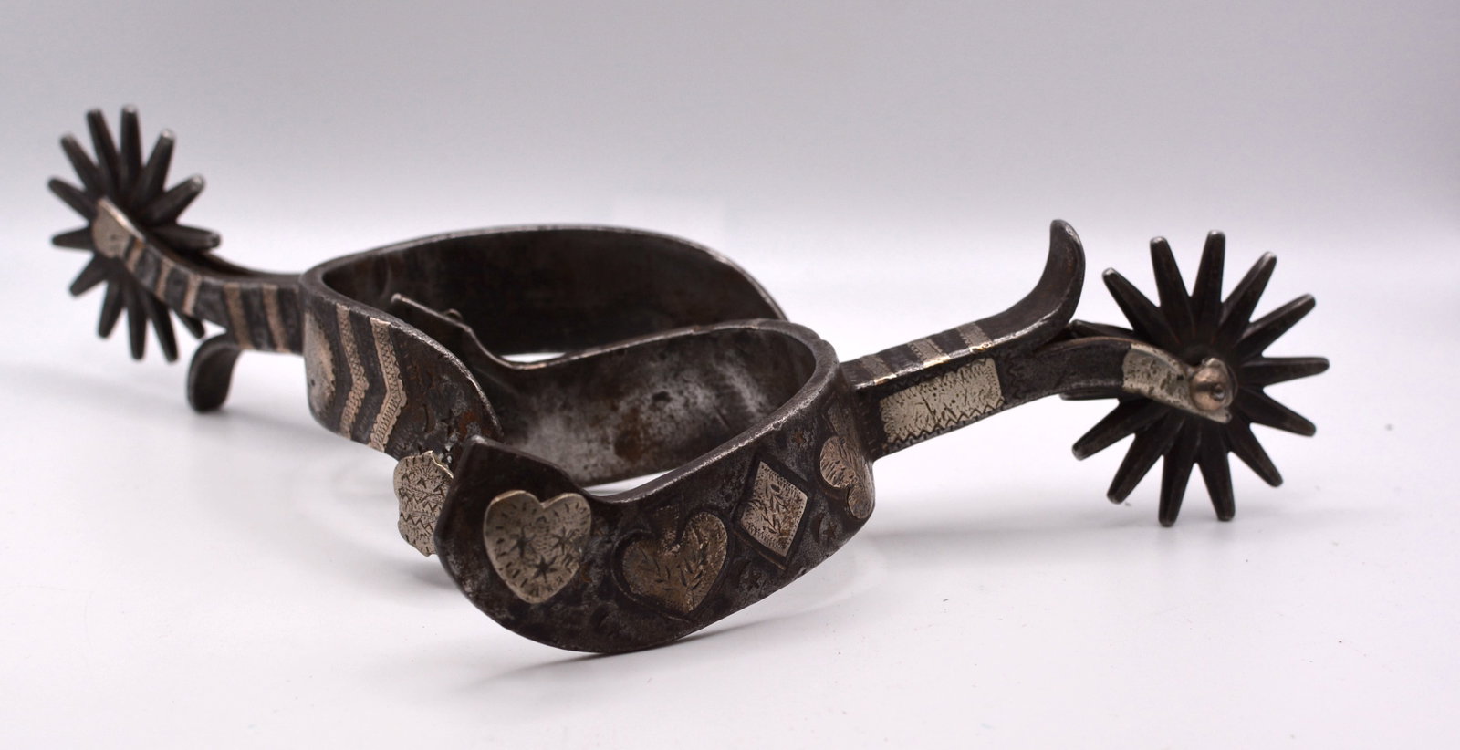 Antique Western Cowboy Spurs with Silver Inlay & Card Suit Decoration: Fine pair of antique hand-forged iron cowboy spurs featuring decorative silver inlay and applied motifs depicting hearts, diamonds and other playing-card suit designs. The shaped heel bands display