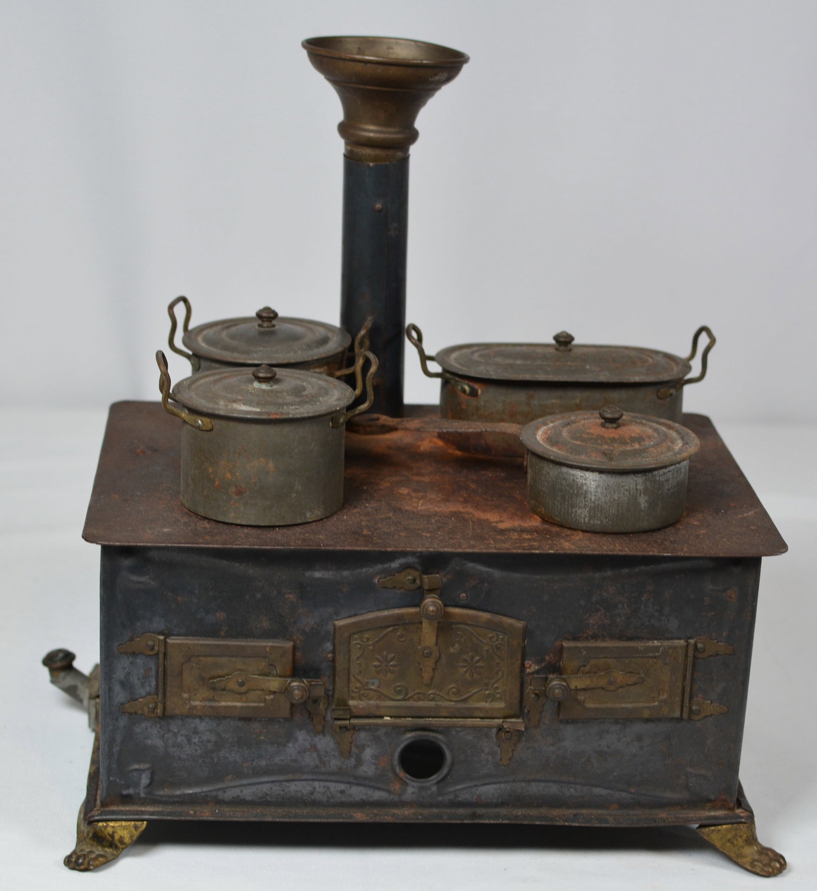 Antique Miniature Tin Toy Cook Stove with Pots & Pans: Early miniature tin toy cook stove featuring a black-painted metal body with ornate brass-tone oven doors, decorative hardware, paw feet, and a tall stovepipe with flared top. Complete with an