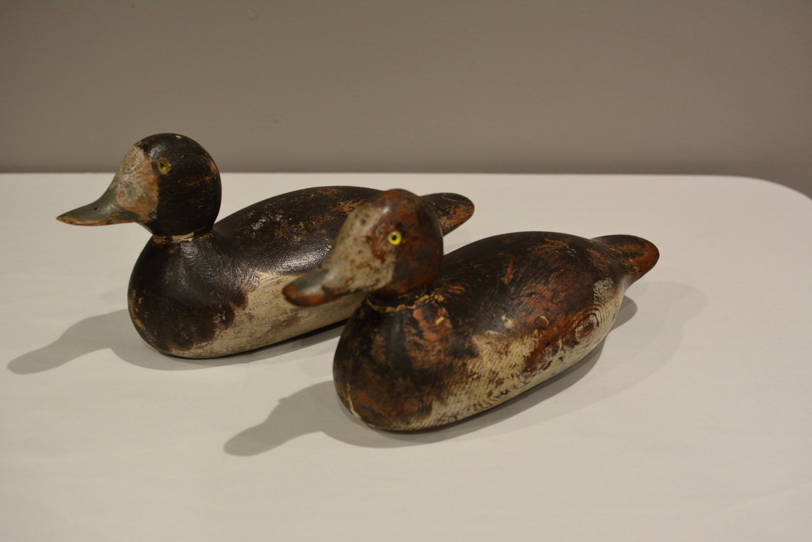 Pair of Early Hand-Carved & Painted Wooden Duck Decoys: Pair of early hand-carved wooden duck decoys with glass eyes and well-worn original-style painted surfaces. Both exhibit strong working-decoy character with extensive paint loss, rubbing, scratches,