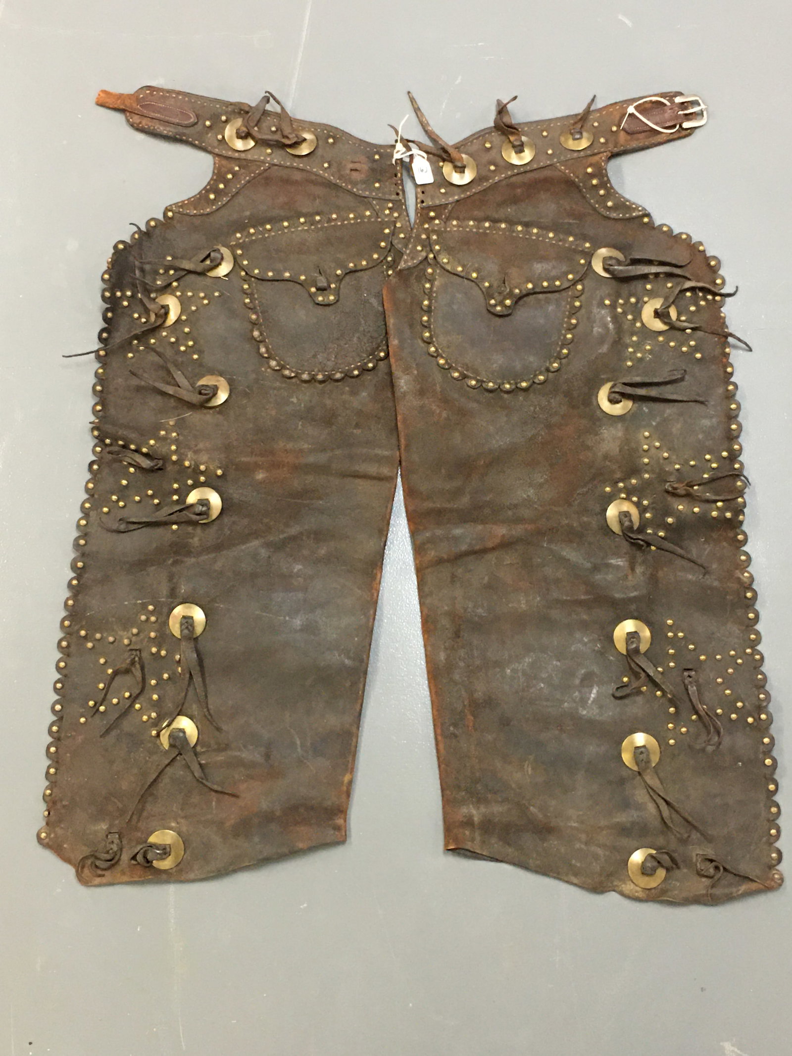 R.T. Frazier Shotgun Chaps: R.T. Frazier Shotgun Chaps. Studded stars down sides with outlines on the pockets. Missing one of the original 20 Conchos. Marked "R.T. Frazier Pueblo Colo.". Belt strap is broken and no center