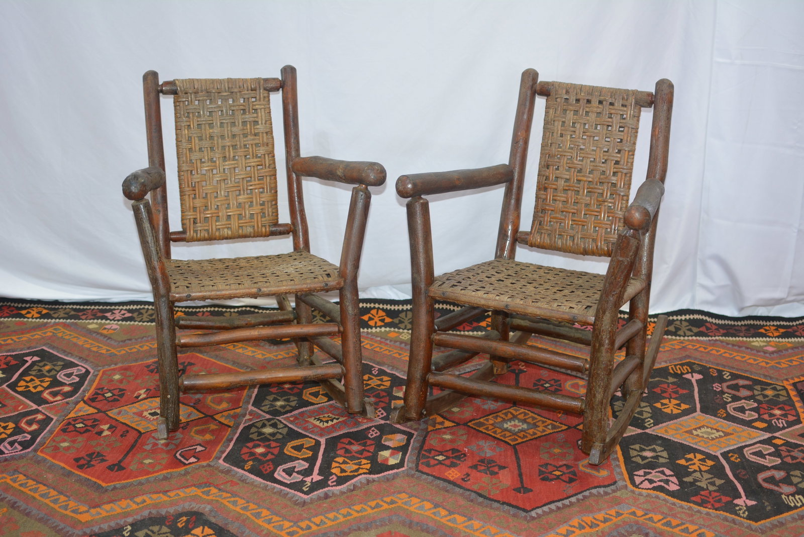 Pair of Early Old Hickory-Style Woven Rocking Chairs: Pair of early rustic hickory rocking chairs featuring natural hickory pole frames with woven splint seats and rectangular woven backs. Each has substantial branch-form arms, double side stretchers