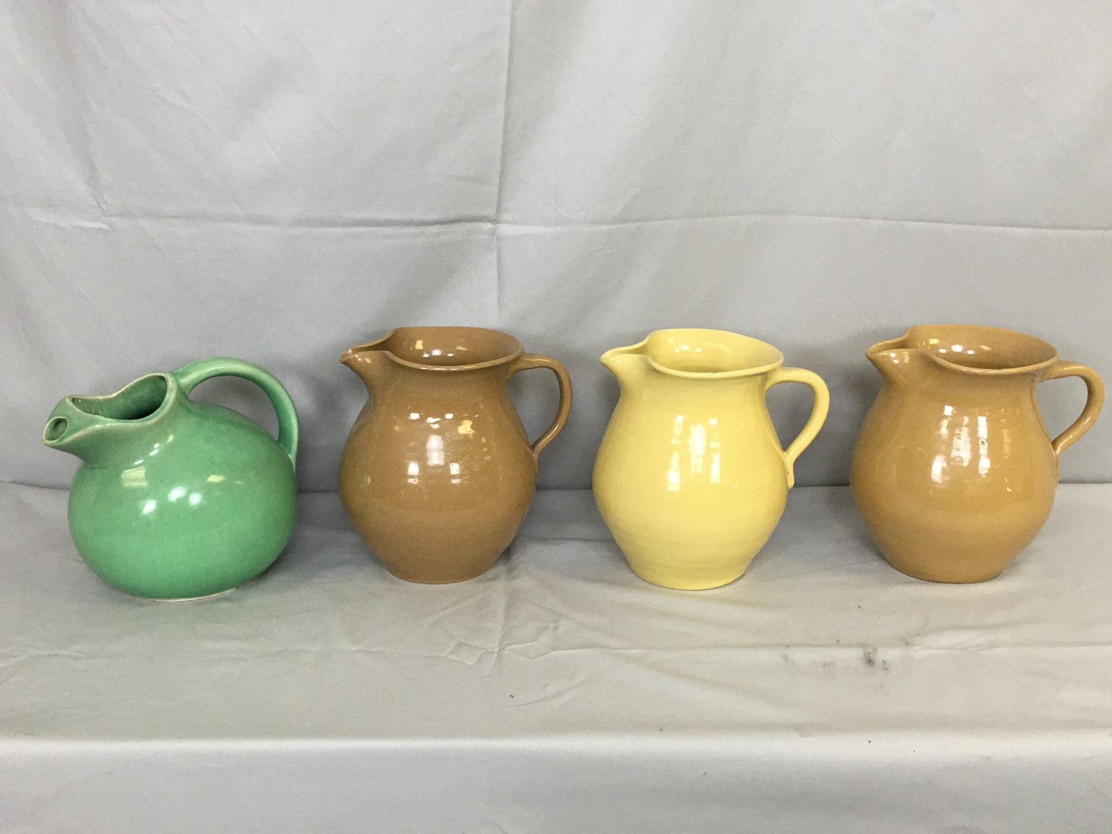 Four Glazed Pottery Pitchers: Four Glazed Pottery Pitchers. (3) pinched spout form, in yellow & brown; and rounded green pitcher, marked USA. Tallest 7.5"H