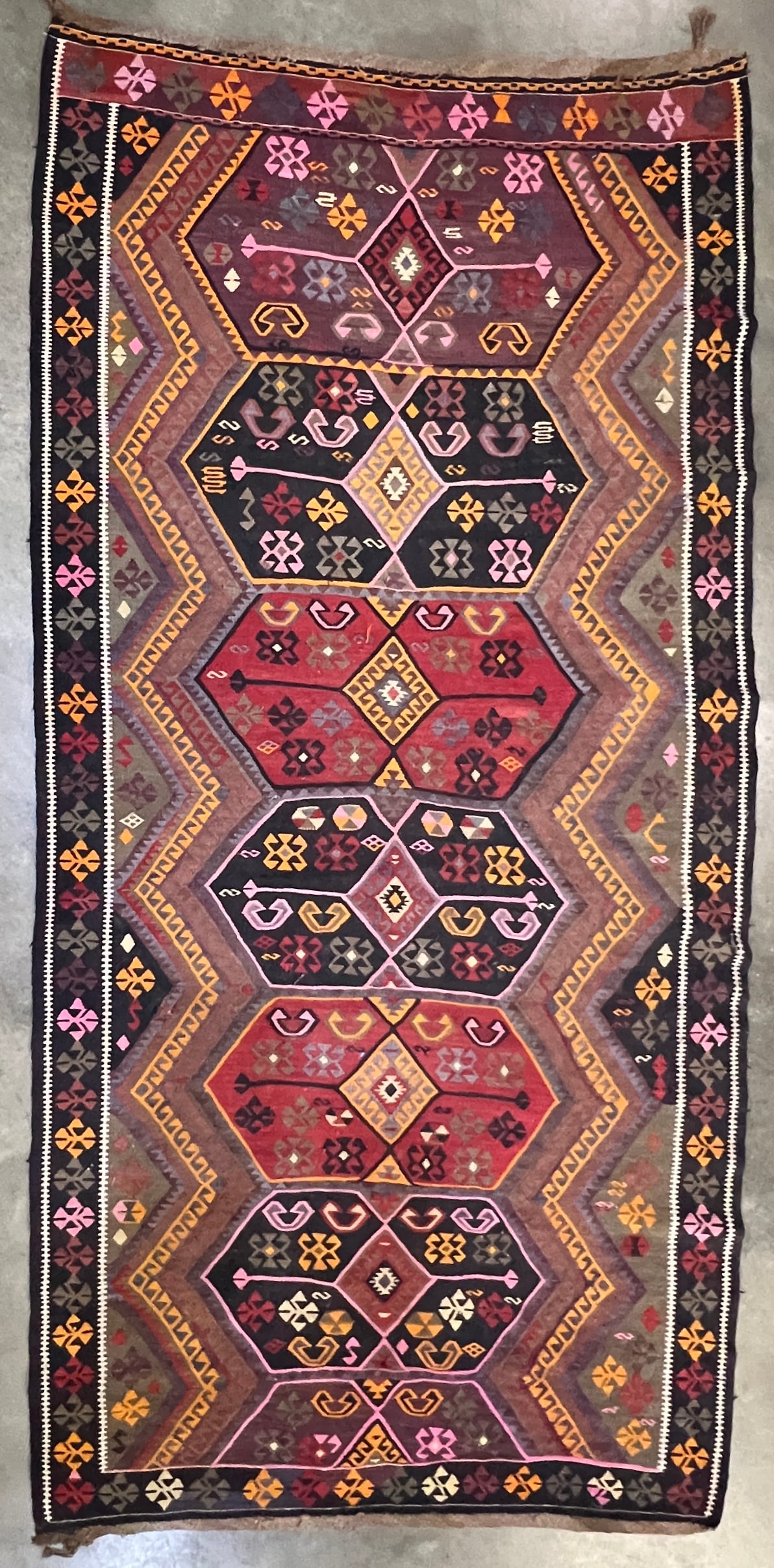 Large Antique Handwoven Anatolian Kilim Rug: Large handwoven flatweave kilim featuring a bold repeating geometric medallion design in red, black, muted purple, olive, pink, cream, and golden yellow. The field is surrounded by multiple geometric 