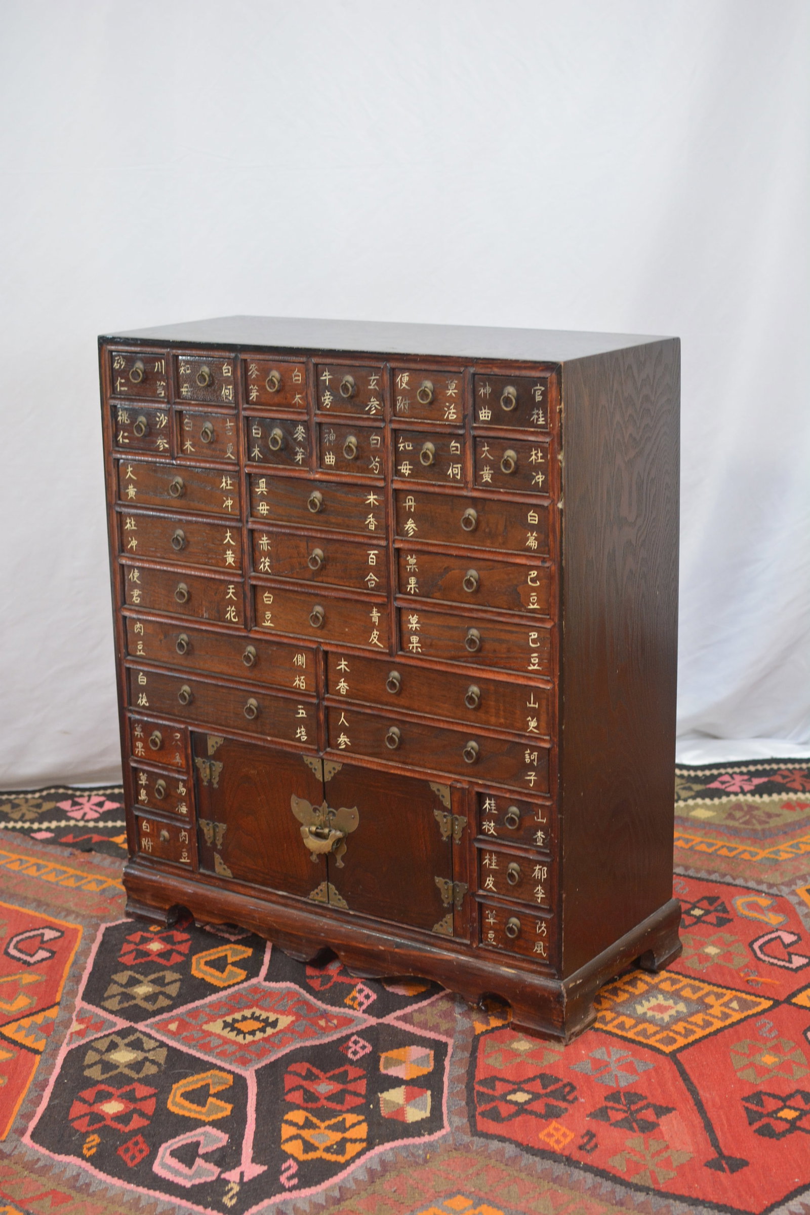 Wooden Apothecary Chest: Traditional wooden apothecary chest, multiple small drawers with Chinese character labels, lower cabinet doors with brass butterfly hardware, dark wood finish.