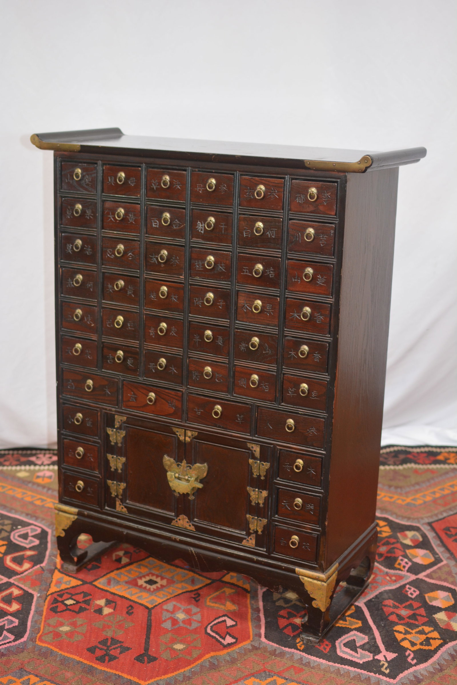 Traditional Wooden Apothecary Chest: Traditional apothecary chest crafted from dark wood, featuring numerous small drawers with brass ring pulls and Chinese character labels. includes a central cabinet with butterfly-shaped brass hardwar