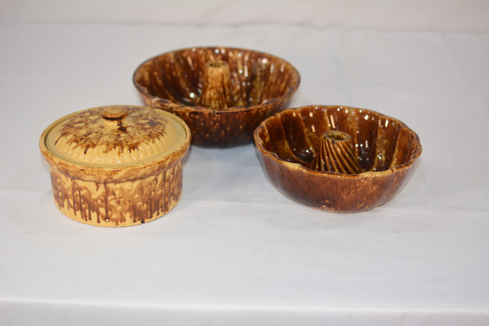 Rockingham Glaze Baking Set: Rockingham set featuring two fluted tube pans and one lidded casserole dish. Each piece displays a distinctive brown drip glaze over a cream-colored base.