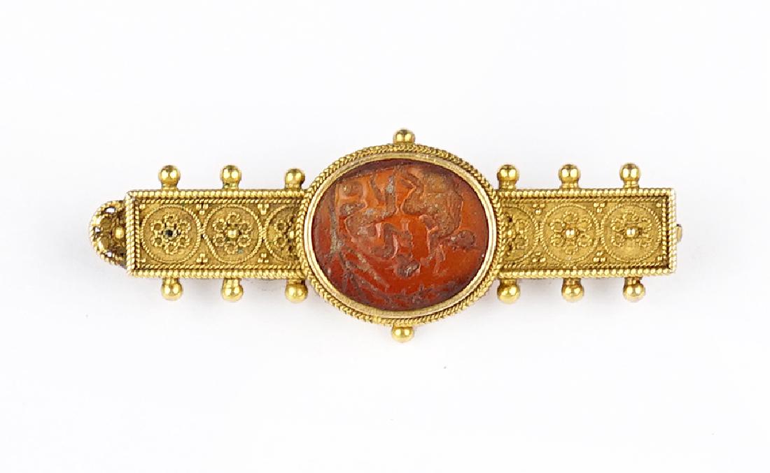 A Victorian Egyptian Revival Brooch.: A Victorian Egyptian Revival Brooch. 18 karat yellow gold brooch containing an intaglio carnelian depicting two figures 3.7 grams .5" x 1.5"