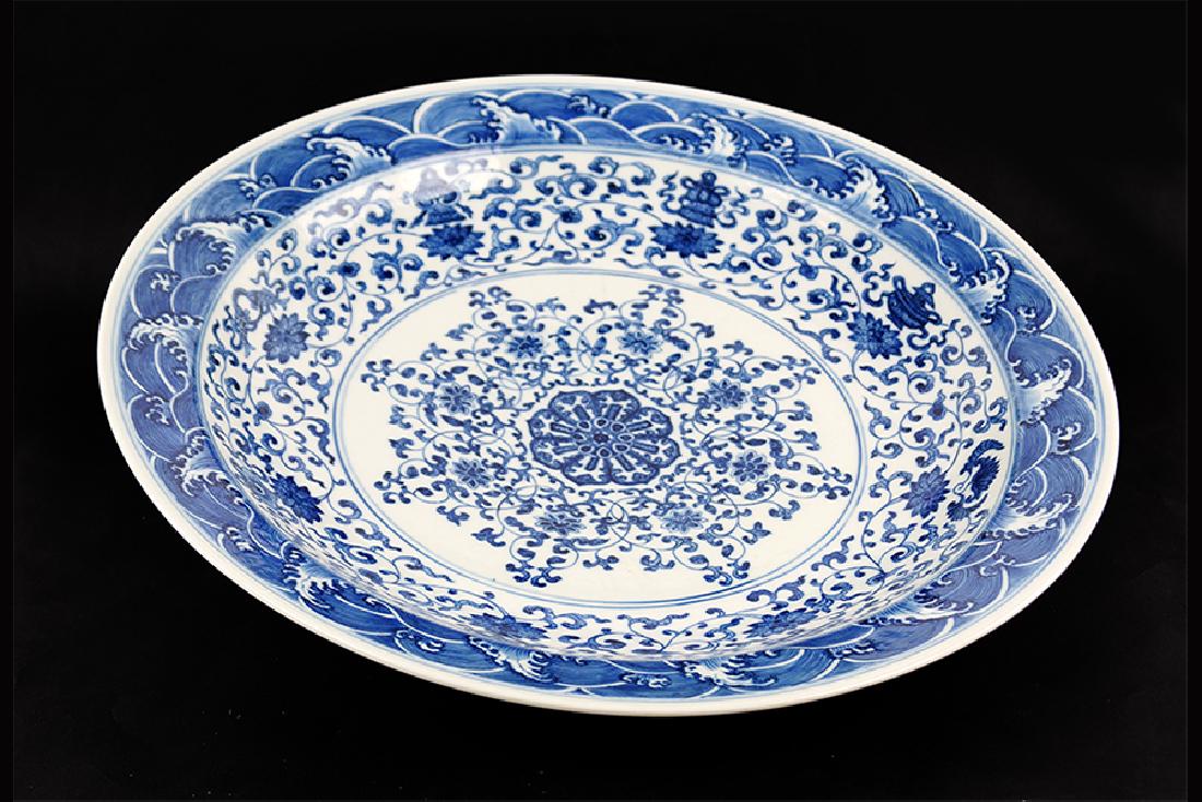 A Chinese Blue and White Porcelain Charger.: A Chinese Blue and White Porcelain Charger. Bearing a decoration of lotus flowers within the bed, the eight auspicious symbols and waves on the rim, and pomegranates on the underside. With an undergla