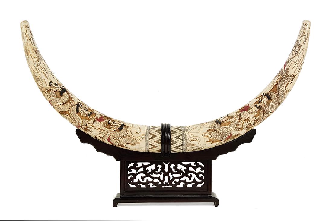 A Pair of Ox Bone Veneer Tusk Forms.: A Pair of Ox Bone Veneer Tusk Forms. Two ox bone tiled tusk forms decorated with dragons throughout. Together with a carved wood display stand Each length: 35"