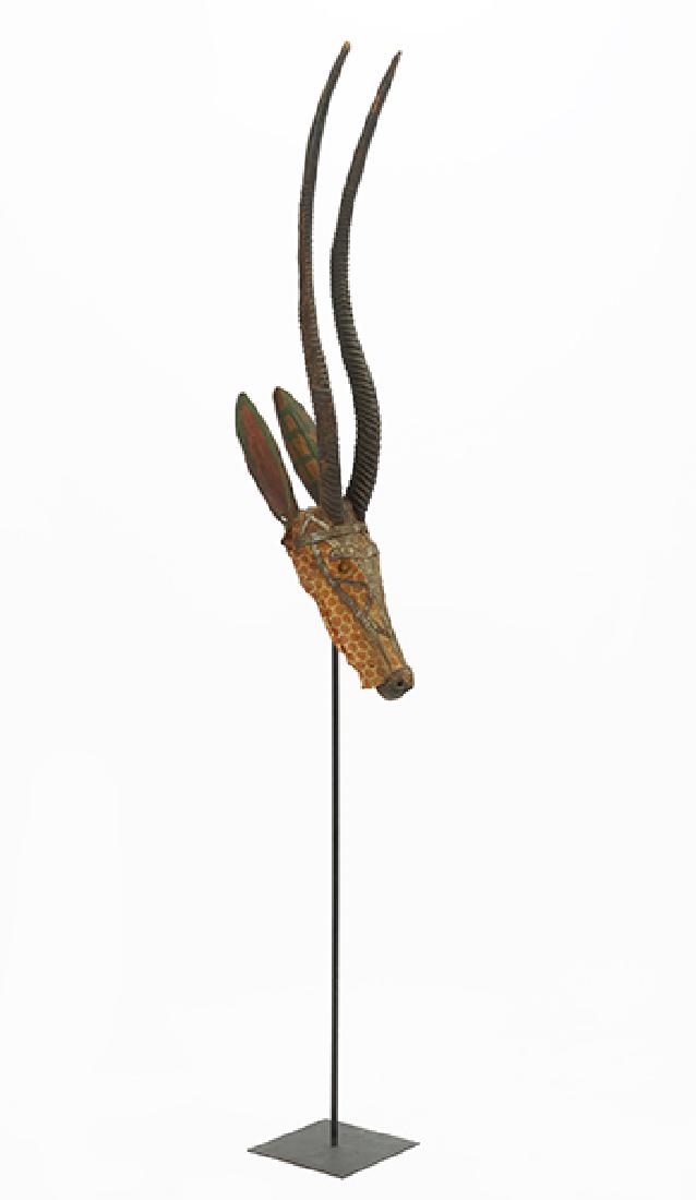 An African Mask Depicting a Gazelle.: An African Mask Depicting a Gazelle. A carved and painted wood mask with cloth overlay and metal mountings. Mounted to a black metal stand Mask height: 49.5" With stand: 88.5"
