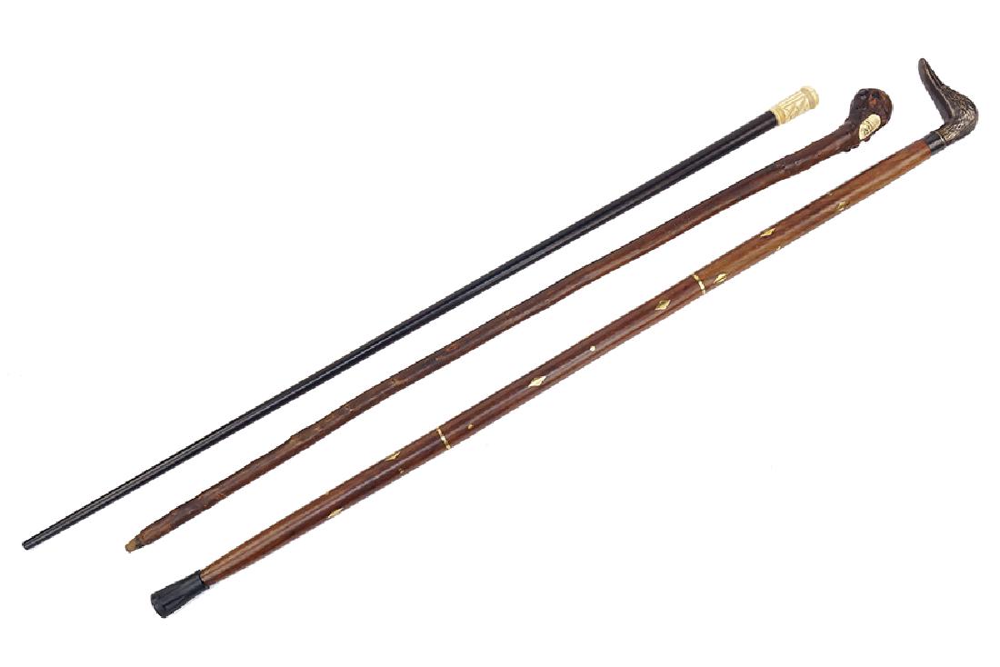 Three Walking Sticks / Canes.: Three Walking Sticks / Canes. One ebonized with a carved bone handle, one burl with an inset carved bone tile, and one with brass inlay and a duck form handle Tallest: 37"