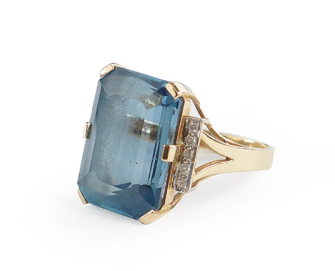 A Blue Topaz and Diamond Ring.: A Blue Topaz and Diamond Ring. 14 karat yellow gold mounting contains one prong set emerald cut blue topaz which is approximately 17 carats. Flanking the topaz are ten round brilliant diamonds Size: 5