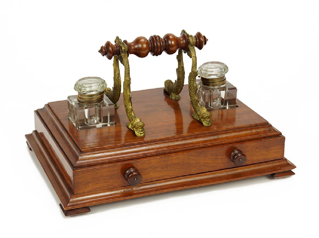 A Double Inkwell Desk Set.: A Double Inkwell Desk Set. With gilt metal dolphin form quill holders, two glass inkwells, and a single drawer below. Together with two brass quills (one with feather) Overall: 7.25" x 12" x 9"