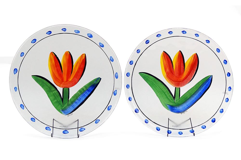 A Pair of Ulrica Hydman Vallien for Kosta Boda Glass: A Pair of Ulrica Hydman Vallien for Kosta Boda Glass Chargers. Round painted glass chargers with a tulip at center and blue dots around the perimeter Diameter: 13 1/4"