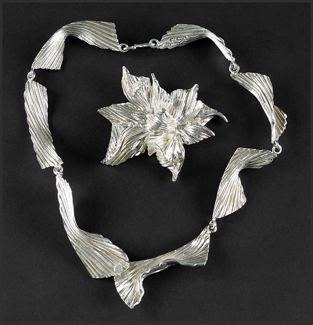 Lynda Benglis (American, B. 1941) A Brooch and: Lynda Benglis (American, B. 1941) A Brooch and Necklace. Sterling silver grooved ribbon form link necklace is stamped on the reverse "L. Benglis 87 AEL 21/350". Sterling silver iris form brooch / pend