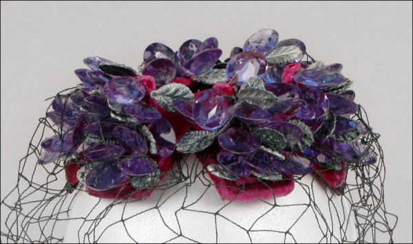 BES-BEN JEWELED HAT.: BES-BEN JEWELED HAT. Pink velvet hat is entirely covered in purple faceted pear shaped beads, green plastic leaves, and a green veil