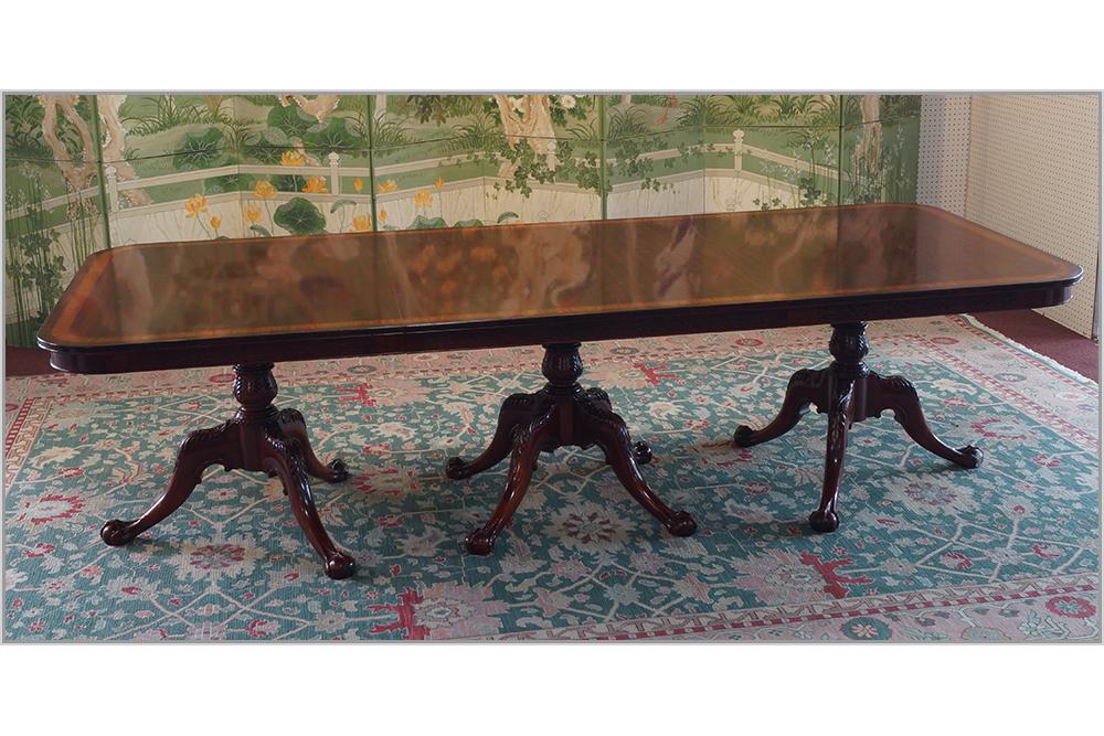 An English Chippendale Style Triple Pedestal Dining: An English Chippendale Style Triple Pedestal Dining Table. Banded mahogany dining table, carved at the apron, and bearing downswept legs that end in ball and claw feet. With two leaves (ea. 48" x 20")