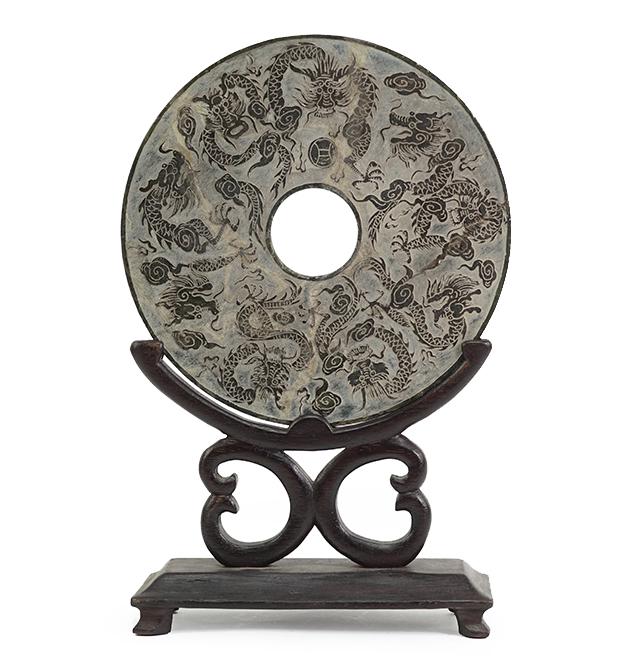 A Chinese Stone Bi Disk.: A Chinese Stone Bi Disk. Bearing a shallow relief of dragons and flaming pearls, with character marks on the verso, set in a fitted wood stand Disk diameter: 8 5/8"