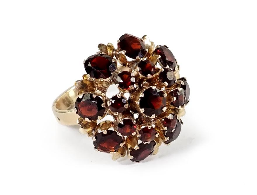 A Garnet Ring.: A Garnet Ring. 18 karat yellow gold ring mounting contains one prong set round garnet at center surrounded by seven prong set round garnets and eight prong set oval garnets Size: 7 3/4 Wt: 7.1 grams