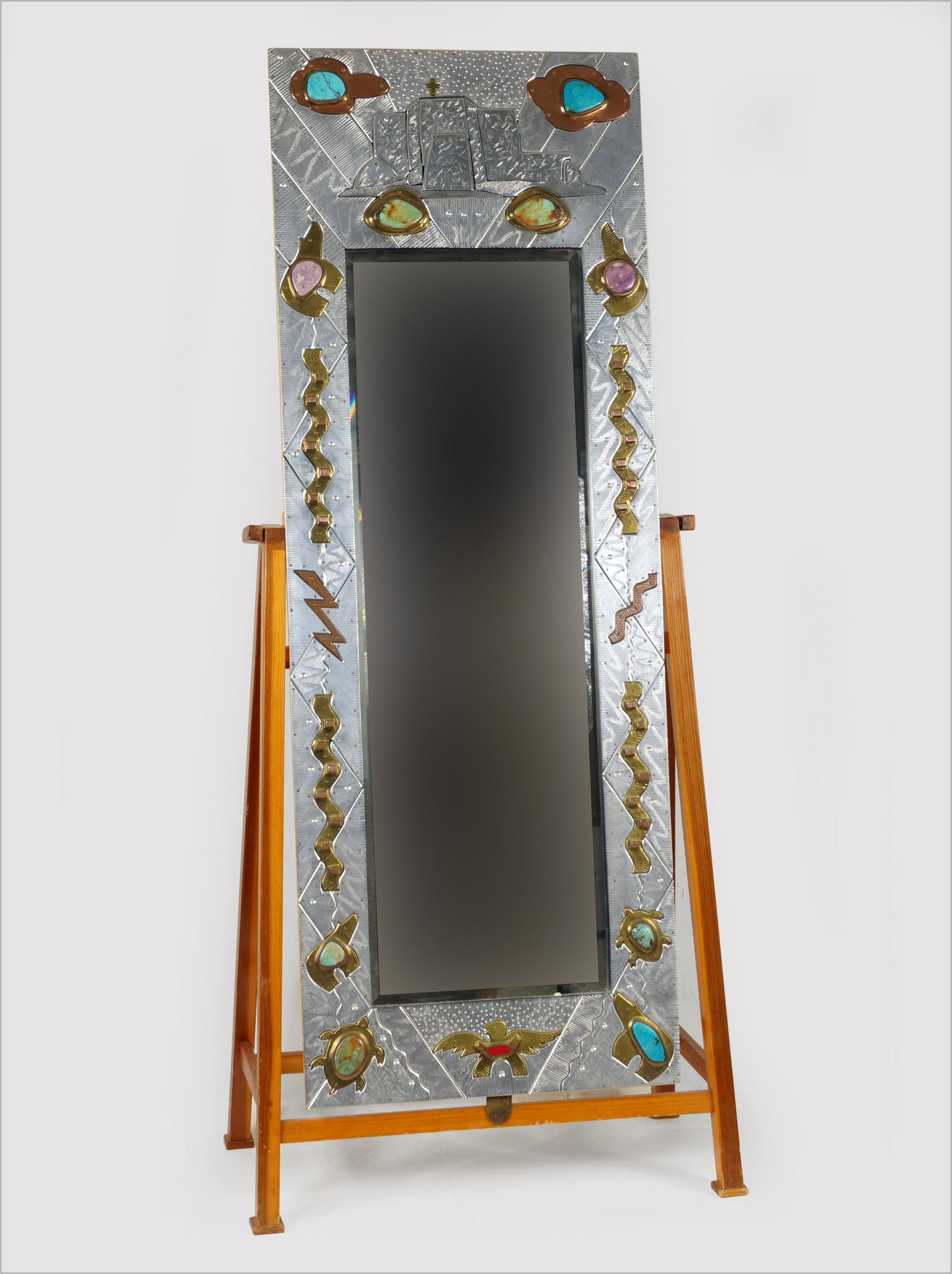 Thom Wheeler (American, B. 1946) Southwest Mirror.: Thom Wheeler (American, B. 1946) Southwest Mirror. Mirror with frame in engraved metal with brass, turquoise and other stones, signed lower right and dated '97, with a wooden stand Frame: 66" x 24"