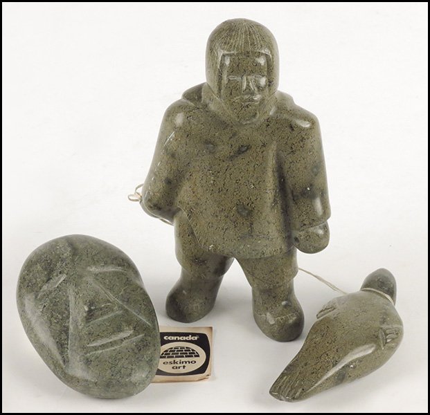 INUIT CARVED STONE FISHERMAN FIGURE WITH A SEAL.: INUIT CARVED STONE FISHERMAN FIGURE WITH A SEAL. Bottom signed in Inuit, dated 1980. Together with an Inuit carved stone head Height 7.5"