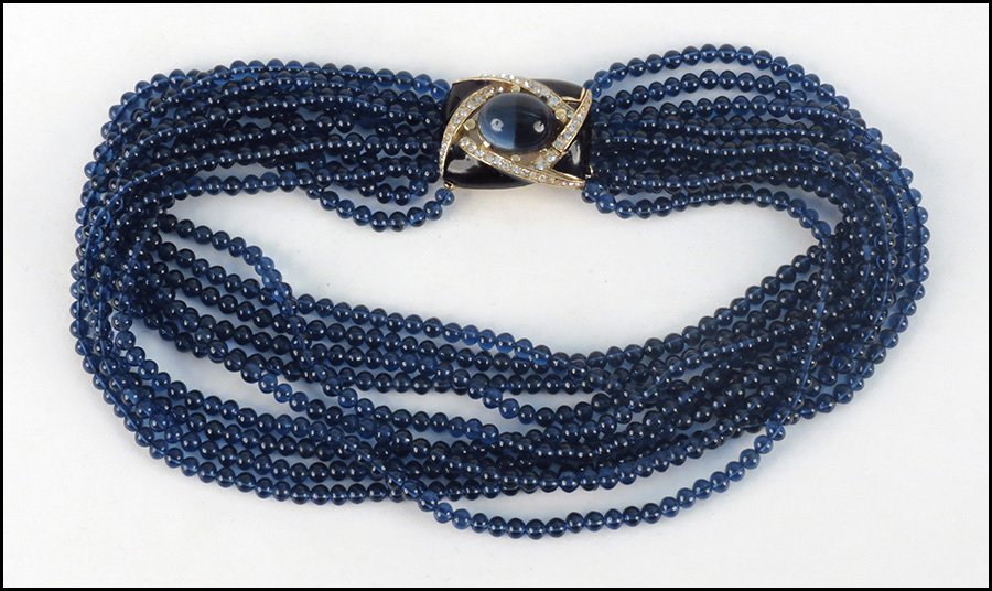 CINER TORSADE NECKLACE.: CINER TORSADE NECKLACE. Comprised of ten strands of blue glass beads, leading into a white rhinestone, enamel, and blue faux cabochon clasp Length: 17.5"