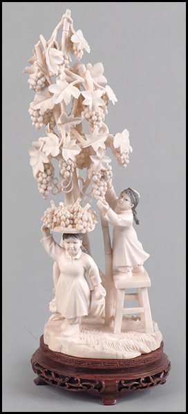 CARVED IVORY FIGURAL GROUP OF TWO YOUNG GIRLS PICKING: CARVED IVORY FIGURAL GROUP OF TWO YOUNG GIRLS PICKING GRAPES. Raised on a 1.5" wood base. One girl stands upon a ladder using scissors to cut grapes from the vine while the other carries a platter of 