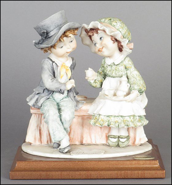 GIUSEPPE ARMANI 'TEA TIME' FIGURAL GROUP.: GIUSEPPE ARMANI 'TEA TIME' FIGURAL GROUP. Depicting a boy and girl drinking tea. Signed on the sculpture. Copyright Florence 1992. Bearing the Capodimonte 'N' crown stamp. Raised on a wood base (1'' x