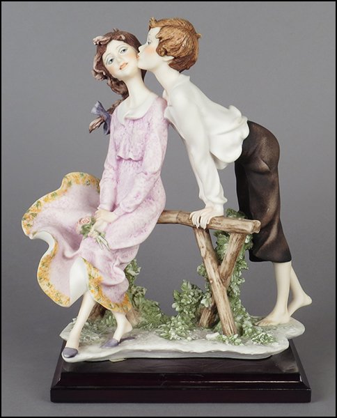 GIUSEPPE ARMANI 'WILD FLOWERS' FIGURAL GROUP.: GIUSEPPE ARMANI 'WILD FLOWERS' FIGURAL GROUP. Depicting a boy kissing a girl on the cheek. Signed on the sculpture. Copyright Florence 1990. Bearing the Capodimonte 'N' crown stamp. Raised on a wood b