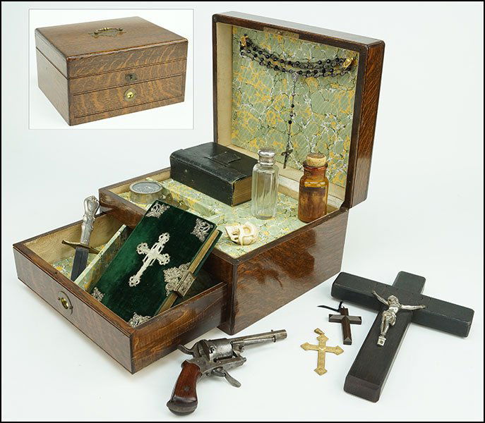 A 19TH CENTURY VAMPIRE KILLING KIT.: A 19TH CENTURY VAMPIRE KILLING KIT. Comprising a prayer book, rosary, crucifix, bible, carved bone skull form netsuke, prayer medals, a knife, and other. All contained in an oak lift top box with sing
