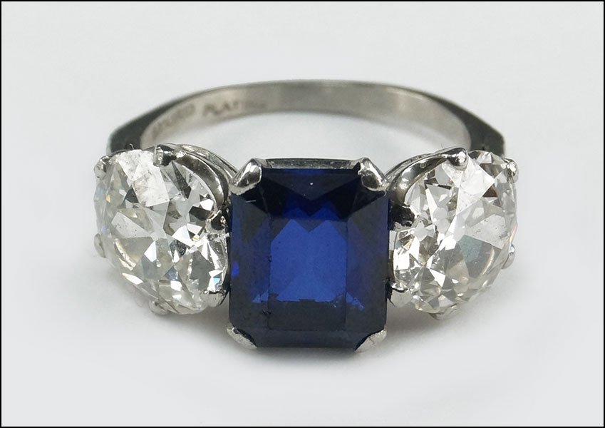 A PLATINUM, DIAMOND, AND SYNTHETIC SAPPHIRE RING.: A PLATINUM, DIAMOND, AND SYNTHETIC SAPPHIRE RING. Containing one synthetic emerald cut sapphire which is approximately 3.75 carats. Flanking the centrak stone are two Old European cut diamonds. One di